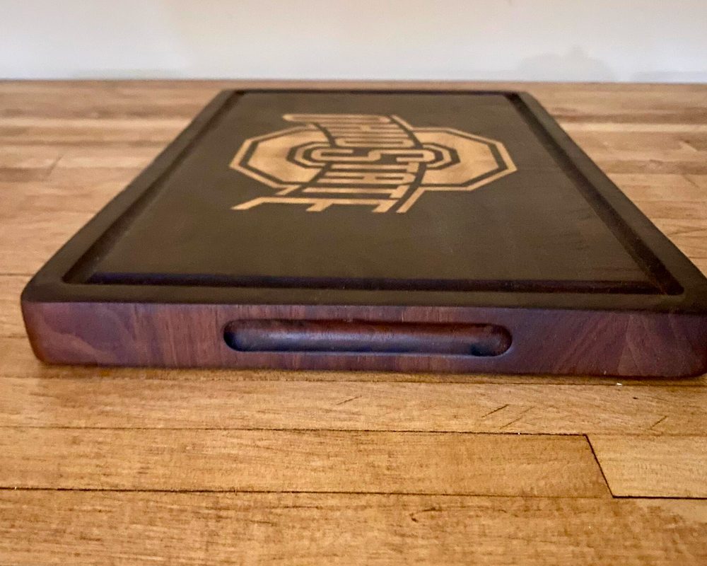 Wooden cutting board with engraved logo design.
